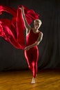 Young woman in red unitard swirling red fabric in studio. Royalty Free Stock Photo