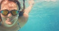 Young woman in reflective swimming glasses swim under water in sea, sun lit bubbles over her face, empty space right side Royalty Free Stock Photo