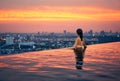 Young woman relax in swimming pool on roof top during amazing sunset and enjoy cityscape Royalty Free Stock Photo