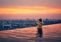 Young woman relax in swimming pool on roof top during amazing sunset and enjoy cityscape Royalty Free Stock Photo