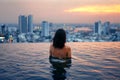 Young woman relax in swimming pool on roof top during amazing sunset and enjoy cityscape Royalty Free Stock Photo