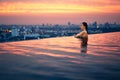 Young woman relax in swimming pool on roof top during amazing sunset and enjoy cityscape Royalty Free Stock Photo