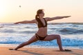 Young woman relaxing on the beach, meditating in warrior asana, at sunset or sunrise and sea Or ocean background, close Royalty Free Stock Photo