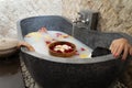 Young woman relaxing in black stone bath with tropical flowers and rose petals. Skin treatment, luxury spa concept Royalty Free Stock Photo