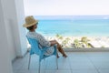 Young woman relaxing in chair on balcony of beachfront hotel or apartment