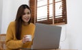 Young woman relaxing and drinking cup of hot coffee or tea using laptop computer on chair.woman checking social apps and working. Royalty Free Stock Photo