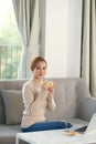 Young woman relaxing and drinking cup of hot coffee or tea using laptop computer Royalty Free Stock Photo