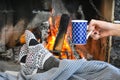 Young woman relaxing in front of cozy fireplace and warming up her feet in woolen socks in country house. Royalty Free Stock Photo