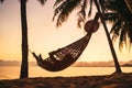 Young woman relaxing in hammock hinged between palm trees on the sand beach at orange sunrise morning time Royalty Free Stock Photo