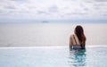 A young woman relaxing in infinity swimming pool looking at a beautiful sea view Royalty Free Stock Photo