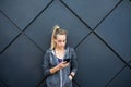 Young woman relaxing after jogging using her smart phone and listening to music and Typing message leaning against black wall. Royalty Free Stock Photo