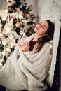 Young woman relaxing with a mug of coffee as she cuddles up in warm blanket on ancient commode. Her eyes closed and