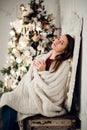 Young woman relaxing with a mug of coffee as she cuddles up in warm blanket on ancient commode. Her eyes closed and