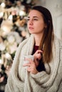 Young woman relaxing with a mug of coffee as she cuddles up in warm blanket on ancient commode. Her eyes closed and