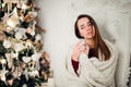 Young woman relaxing with a mug of coffee as she cuddles up in warm blanket on ancient commode. Her eyes closed and