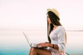 Young woman in straw hat relaxing near waterpool with laptop in the evening Royalty Free Stock Photo
