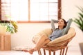 Young woman relaxing in papasan chair near window with blinds at home Royalty Free Stock Photo