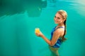 Young woman relaxing in a pool in summer with glass of orange juice. Pretty caucasian blonde girl wearing blue swimsuit Royalty Free Stock Photo