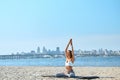 Young woman relaxing practicing yoga and meditation on the sand beach with city background. Sporty girl is sitting in Royalty Free Stock Photo