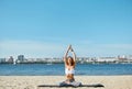 Young woman relaxing practicing yoga and meditation on the sand beach with city background. Sporty girl is sitting in Royalty Free Stock Photo