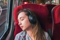 Young woman relaxing or sleeping while listening music in headphones sitting near the window in train Royalty Free Stock Photo