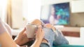 Young woman relaxing on the sofa at home, watching tv and enjoying coffee, top view Royalty Free Stock Photo