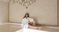 A young woman is relaxing in a traditional hammam, waiting for a Moroccan spa treatment, sitting on a marble bench with her eyes