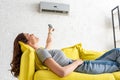 Young woman relaxing under air conditioner and holding remote control Royalty Free Stock Photo