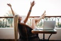 Young woman with raised hands relaxing with laptop computer on a balcony on summer vocation