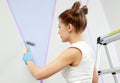 Young woman renovating home painting wall with paint roller and using masking tape while standing on ladder Royalty Free Stock Photo