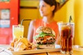 Young Woman In Restaurant Enjoying Tasty Juicy American Beef Burger Menu With Lettuce, Ketchup And Potato Chips