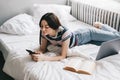 Young woman resting on a bed at home and using laptop computer and smartphone Royalty Free Stock Photo