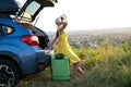Young woman resting on a green suitcase near her car in summer nature. Travel and vacations concept Royalty Free Stock Photo
