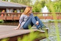 Young woman resting and having fun in the park sitting on a pier over the lake. Royalty Free Stock Photo