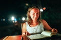 Young woman resting in an outdoor cafe looks menu at the sea on beautiful bokeh lights Royalty Free Stock Photo