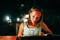 Young woman resting in an outdoor cafe looks menu at the sea on beautiful bokeh lights Royalty Free Stock Photo