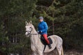 Young woman rider in a blue blazer and sporting a cap for a walk on a white horse Royalty Free Stock Photo