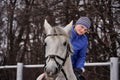 Young woman rider in a blue blazer and sporting a cap for a walk on a white horse Royalty Free Stock Photo