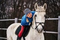 Young woman rider in a blue blazer and sporting a cap for a walk on a white horse Royalty Free Stock Photo