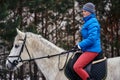 Young woman rider in a blue blazer and sporting a cap for a walk on a white horse Royalty Free Stock Photo