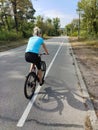 A young woman rides a bicycle along the asphalt road in the park. Active recreation in nature Royalty Free Stock Photo