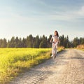 Young woman rides bicycle on dusty country road, afternoon sun shines at her, view from front Royalty Free Stock Photo