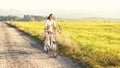 Young woman rides bicycle on dusty country road, afternoon sun shines at her, view from front Royalty Free Stock Photo