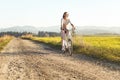 Young woman rides bicycle on dusty country road, smiling, afternoon sun shines at her, view from front Royalty Free Stock Photo