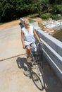 Young woman riding bicycle across river bridge next to tropical park Royalty Free Stock Photo