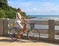 Young woman riding bicycle across river bridge next to tropical park Royalty Free Stock Photo