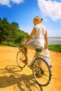 Young woman riding bicycle across river bridge next to tropical park Royalty Free Stock Photo