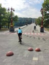 A young woman is riding a bicycle along the asphalt road to the bridge. Active recreation in nature. Rear view Royalty Free Stock Photo