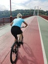 A young woman is riding a bicycle along the asphalt road to the bridge. Active recreation in nature. Rear view Royalty Free Stock Photo