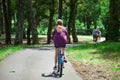 Young woman is riding a blue bicycle in a purple shirt in the park. View from the back. Bike ride in the nature on a sunny summer